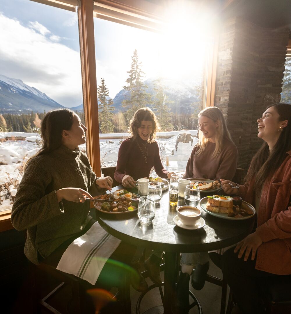 A group of friends enjoy a meal at the Juniper Bistro with a view of Mount Rundle out the window